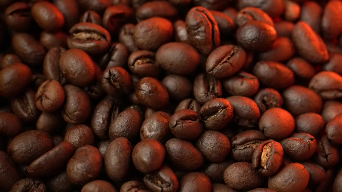 A close-up pile of roasted coffee beans with warm reddish-brown lighting, filling the entire frame.